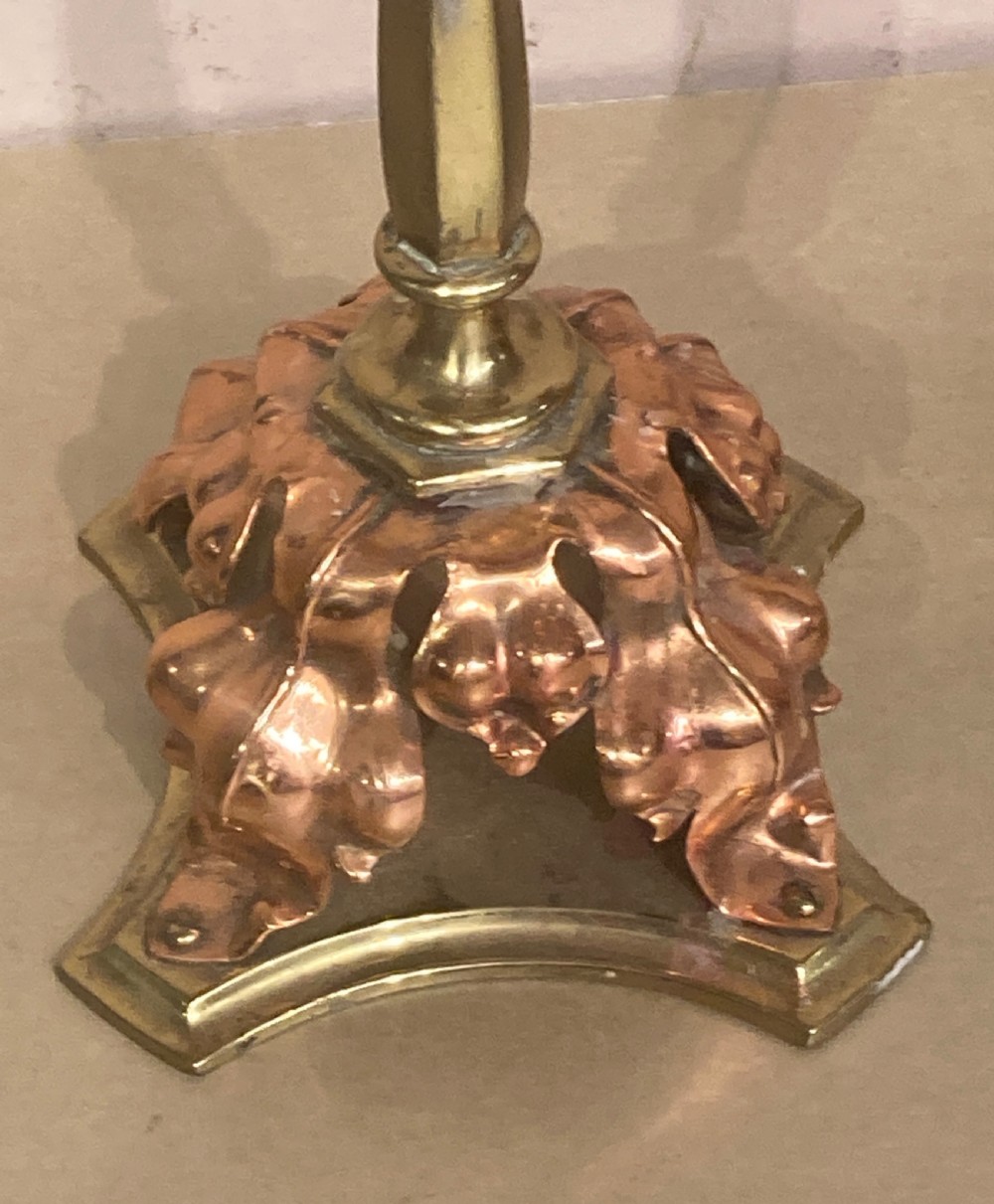 A pair of brass and copper Arts and Crafts candlesticks featuring stylised leaf sconces, slender tapered shafts, and pierced botanical bases. View II