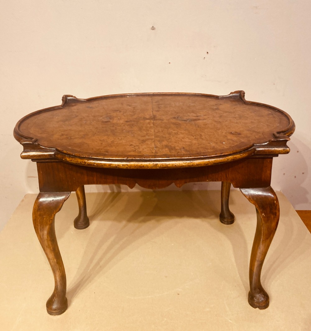 An oval burr walnut coffee table featuring a shaped tray rim and carved cabriole legs ending in pad feet.