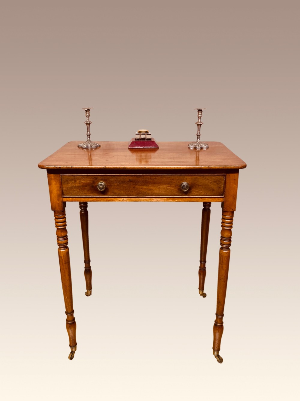 A Georgian mahogany writing table featuring a single drawer with two brass knobs, slender turned legs, and brass castors.