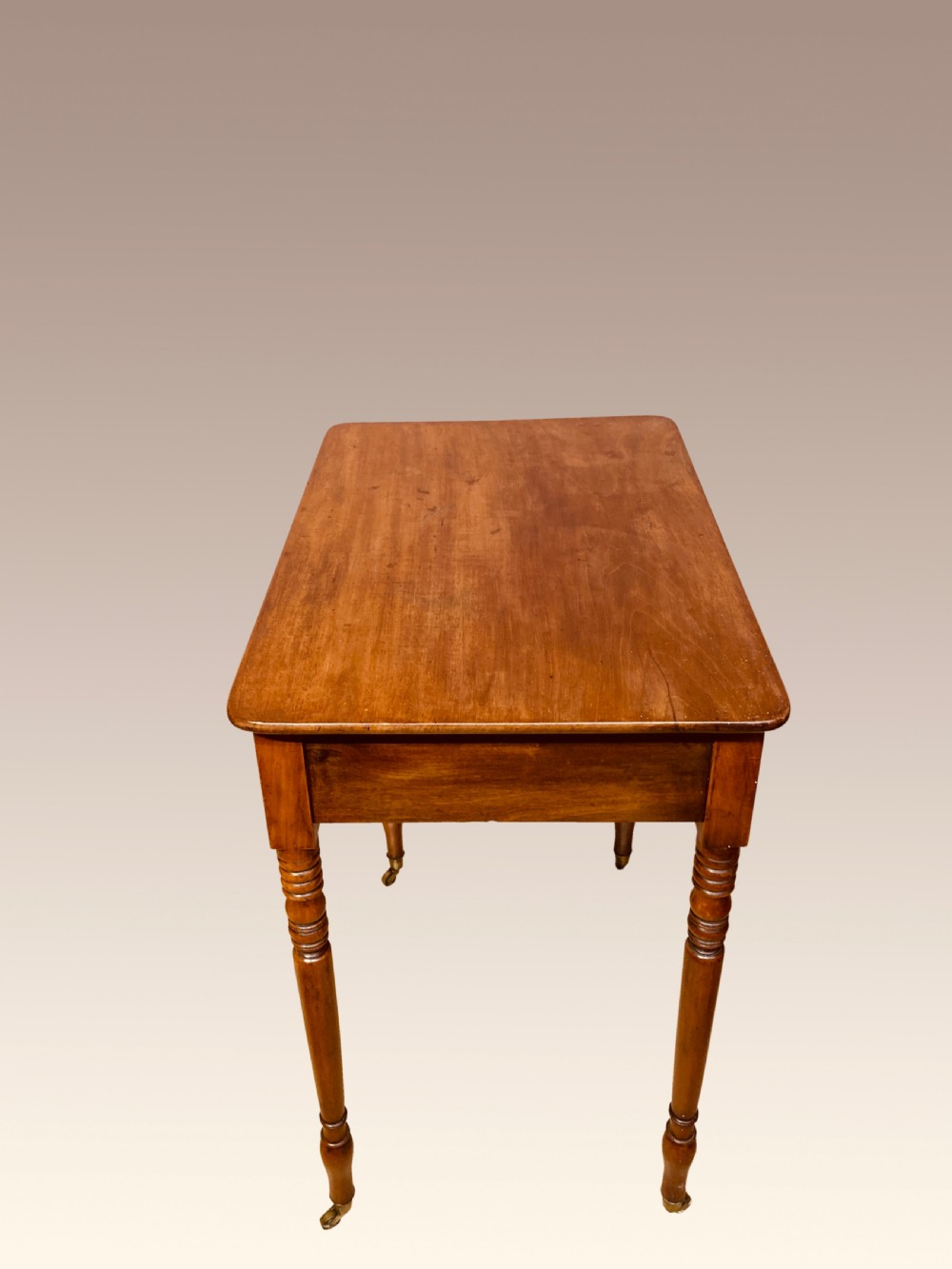A Georgian mahogany writing table featuring a single drawer with two brass knobs, slender turned legs, and brass castors. View II