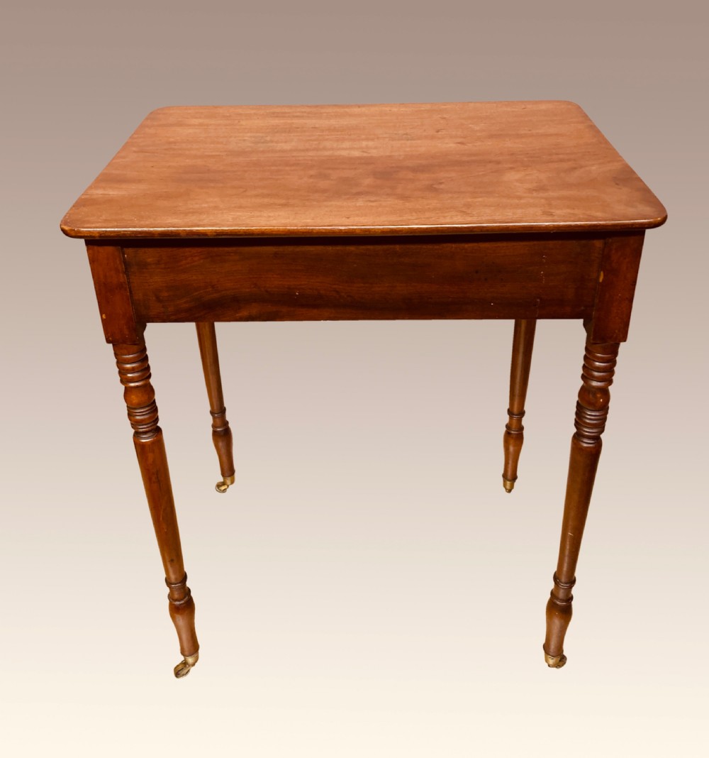 A Georgian mahogany writing table featuring a single drawer with two brass knobs, slender turned legs, and brass castors. View V