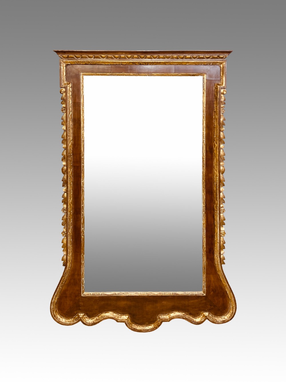 A rectangular 19th-century wall mirror crafted with polished mahogany veneer, bordered by carved gold giltwood trim and featuring a scalloped lower apron.