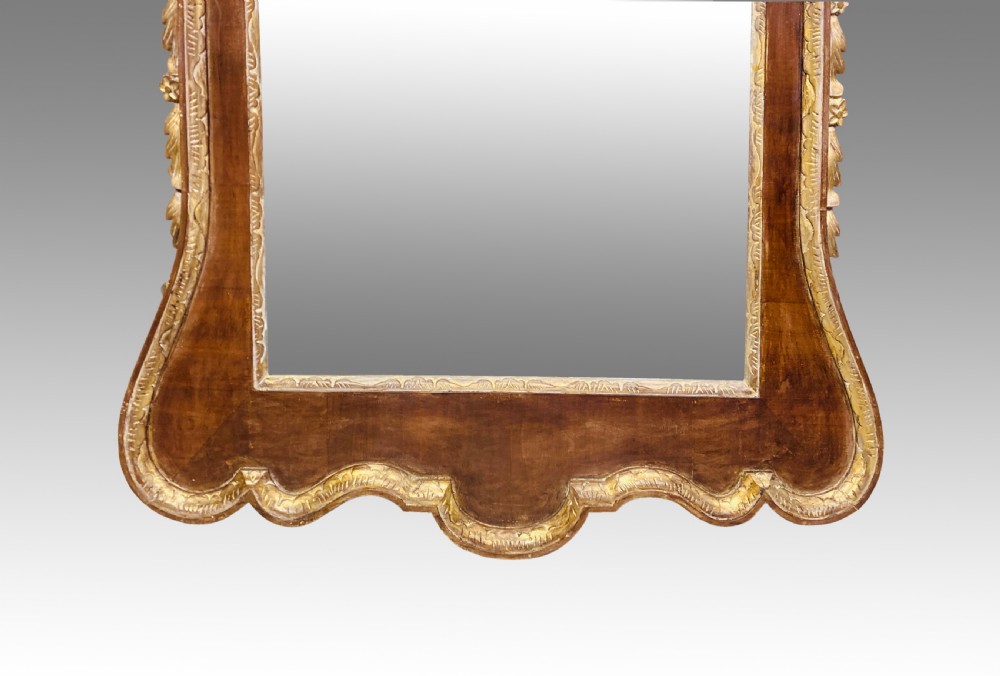 A rectangular 19th-century wall mirror crafted with polished mahogany veneer, bordered by carved gold giltwood trim and featuring a scalloped lower apron. View II