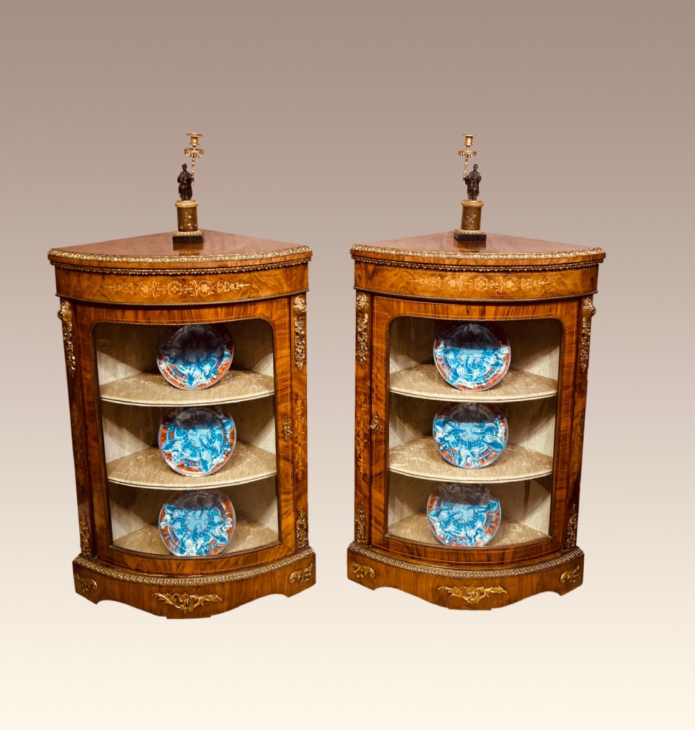 A pair of Victorian inlaid walnut corner cabinets featuring curved glass display doors, decorative floral marquetry, and gilt bronze mounts. View II