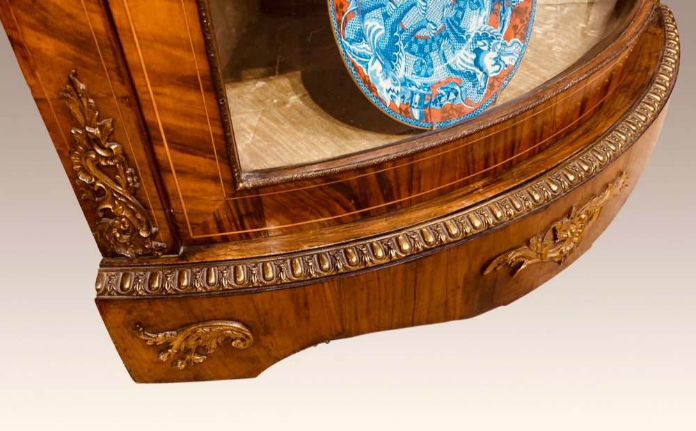 A pair of Victorian inlaid walnut corner cabinets featuring curved glass display doors, decorative floral marquetry, and gilt bronze mounts. View VII