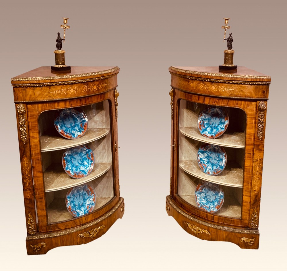 A pair of Victorian inlaid walnut corner cabinets featuring curved glass display doors, decorative floral marquetry, and gilt bronze mounts. View XI