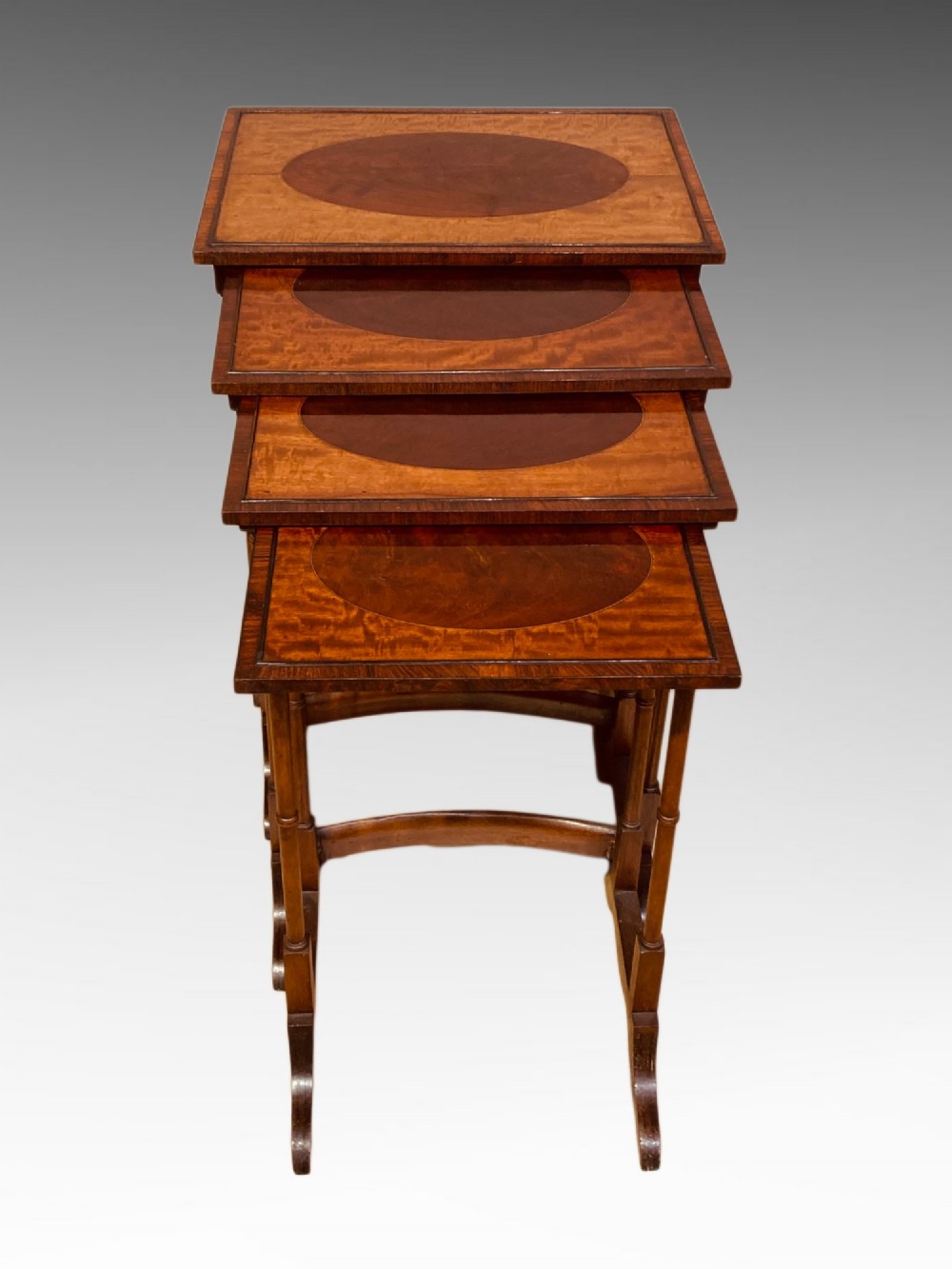 A set of four graduated mahogany nesting tables featuring oval satinwood centre inlays and slim turned dual-spindle legs.