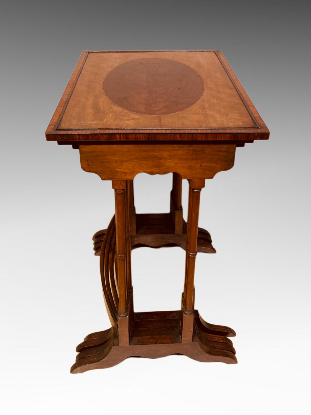 A set of four graduated mahogany nesting tables featuring oval satinwood centre inlays and slim turned dual-spindle legs. View V