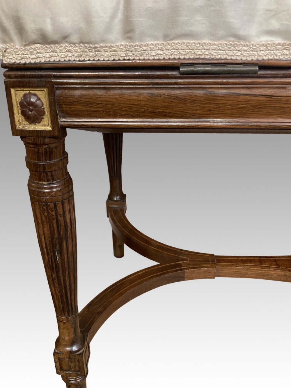 A 19th-century rosewood rectangular music bench featuring a cream upholstered seat, fluted legs, and a gilt decorative central panel on the frieze. View II