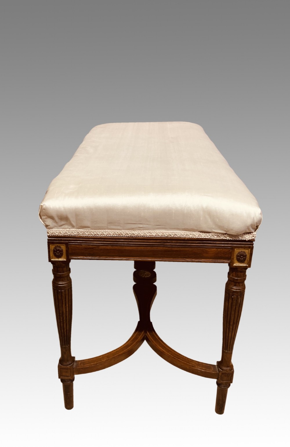 A 19th-century rosewood rectangular music bench featuring a cream upholstered seat, fluted legs, and a gilt decorative central panel on the frieze. View VI