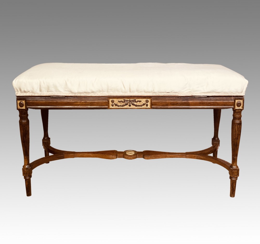 A 19th-century rosewood rectangular music bench featuring a cream upholstered seat, fluted legs, and a gilt decorative central panel on the frieze. View X