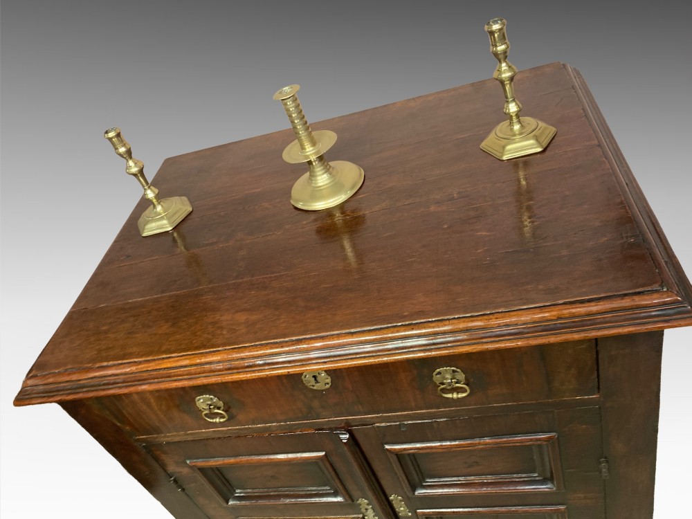 An antique dark brown walnut cupboard with a single top drawer, two fielded panel doors, brass drop handles, and bracket feet. View II