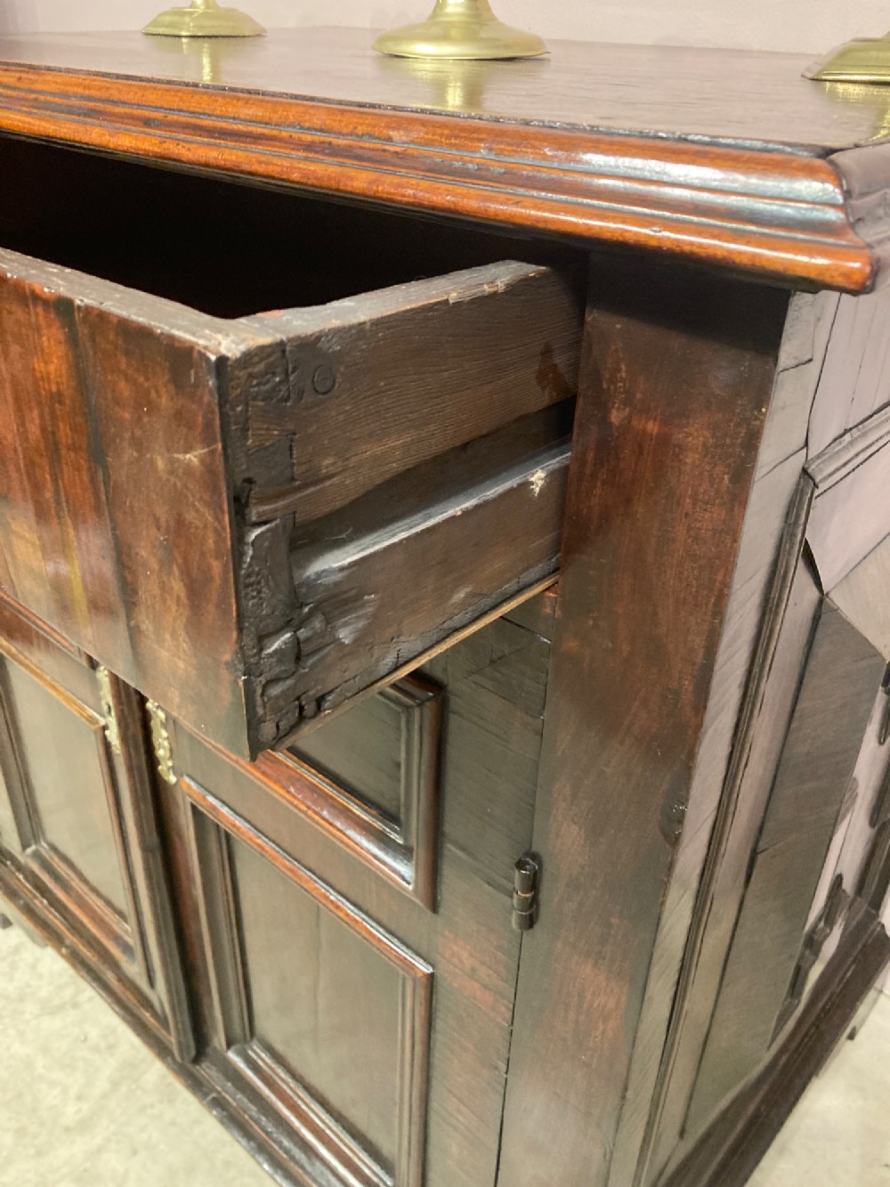 An antique dark brown walnut cupboard with a single top drawer, two fielded panel doors, brass drop handles, and bracket feet. View VI