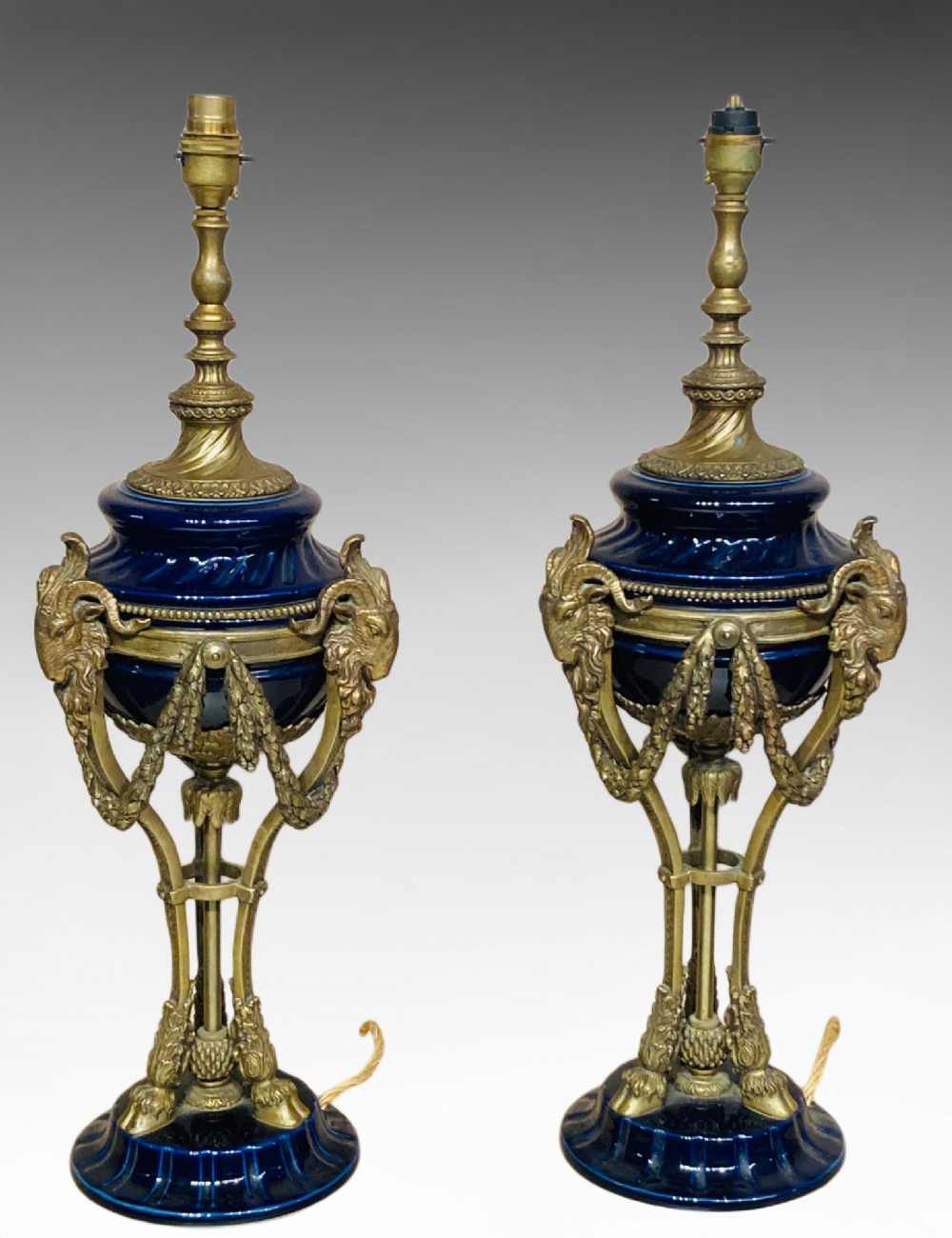 A pair of cobalt blue glazed ceramic urn-shaped table lamps mounted with gilt bronze ram head handles and festoons.