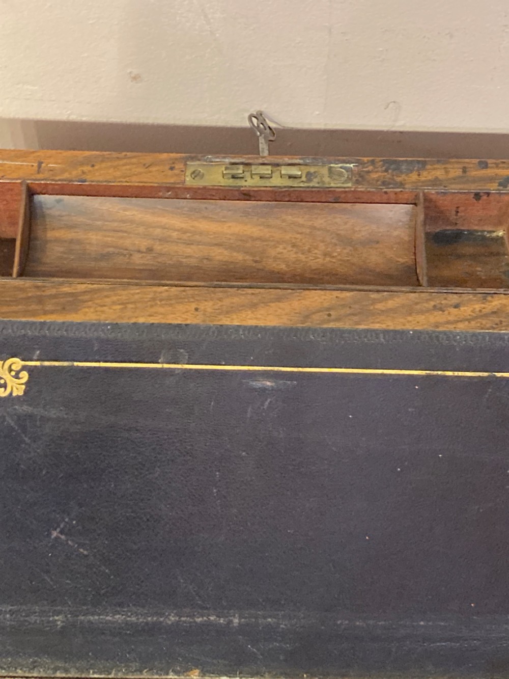 A rectangular Late Georgian burr walnut writing slope box featuring brass edging, an oval brass lid plaque, and a keyhole with key on the front. View VI