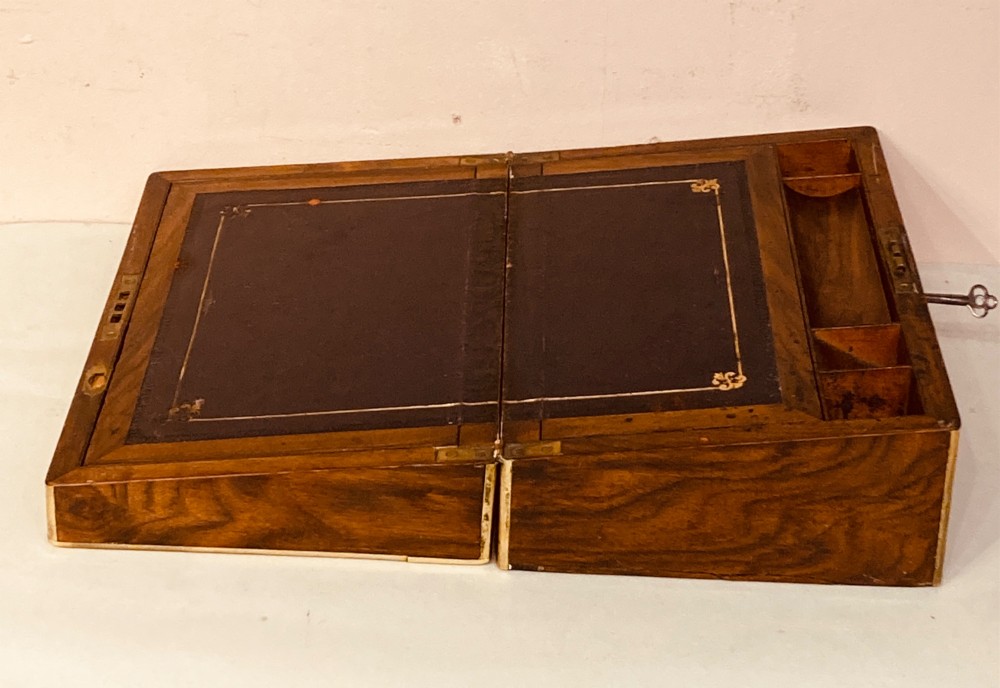 A rectangular Late Georgian burr walnut writing slope box featuring brass edging, an oval brass lid plaque, and a keyhole with key on the front. View IX
