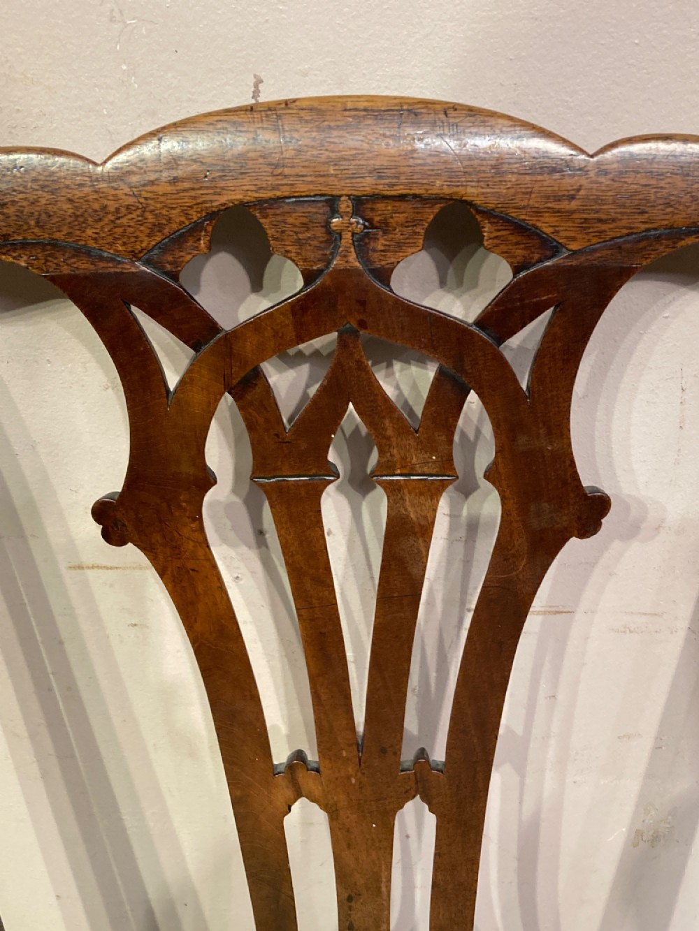 A pair of antique Georgian mahogany side chairs featuring pierced Gothic splat backs, cream upholstered seats, and straight legs connected by stretchers. View II