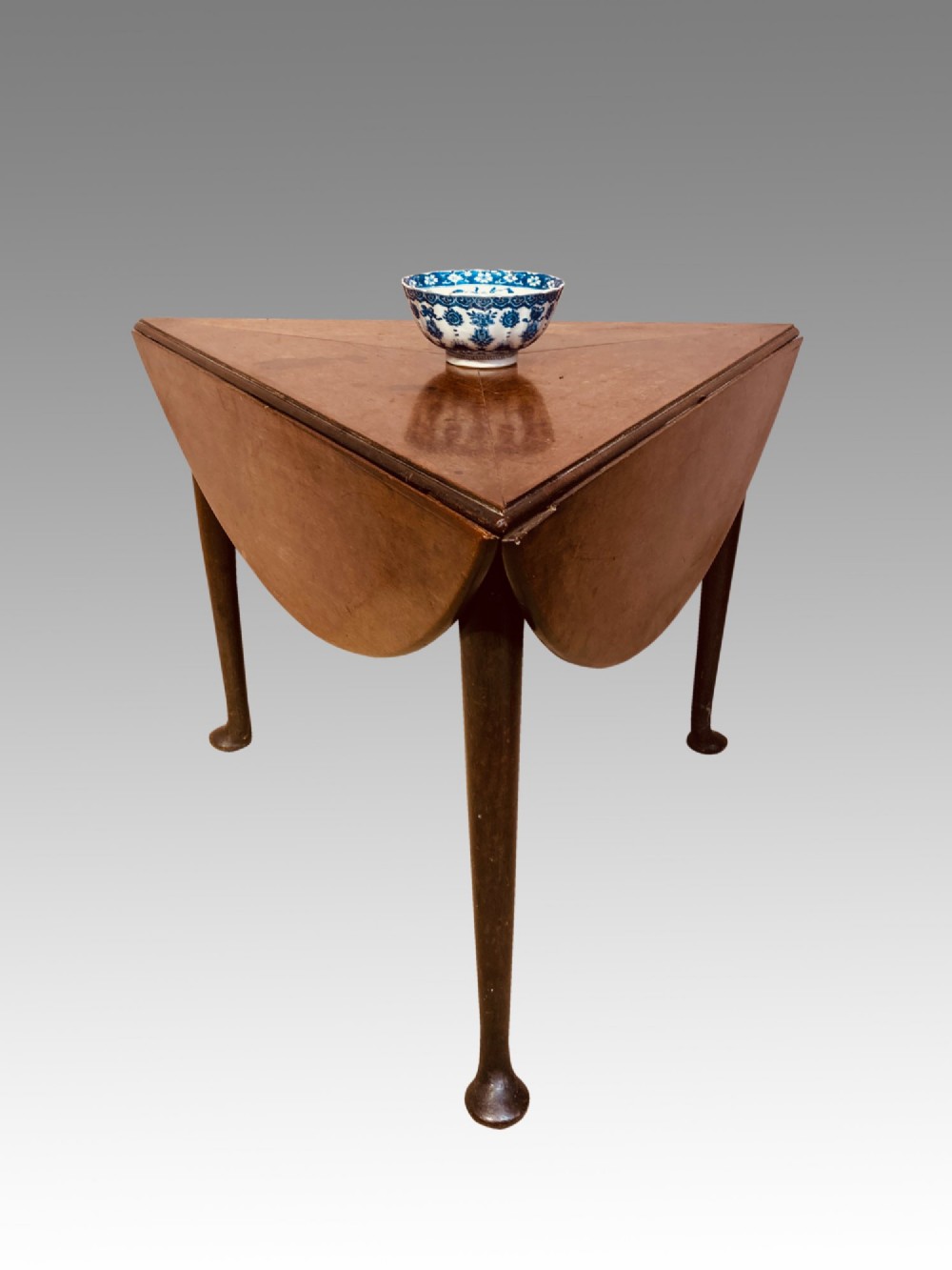 A Georgian red walnut drop-leaf table featuring a triangular top, drop flaps, and turned legs ending in pad feet.