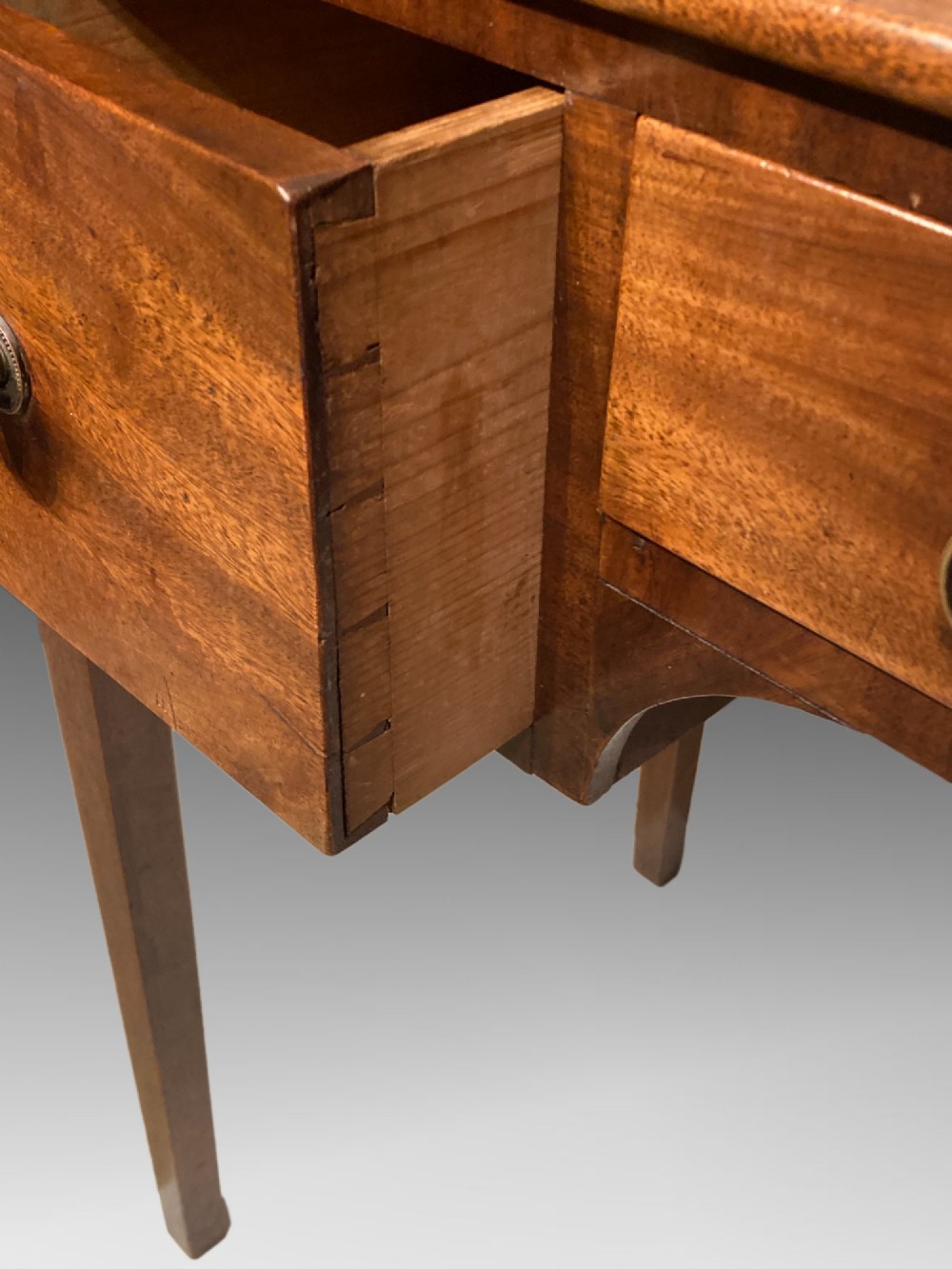 An antique Georgian mahogany side table featuring three drawers, brass knob handles, an upstand gallery back, and straight tapered legs. View IV