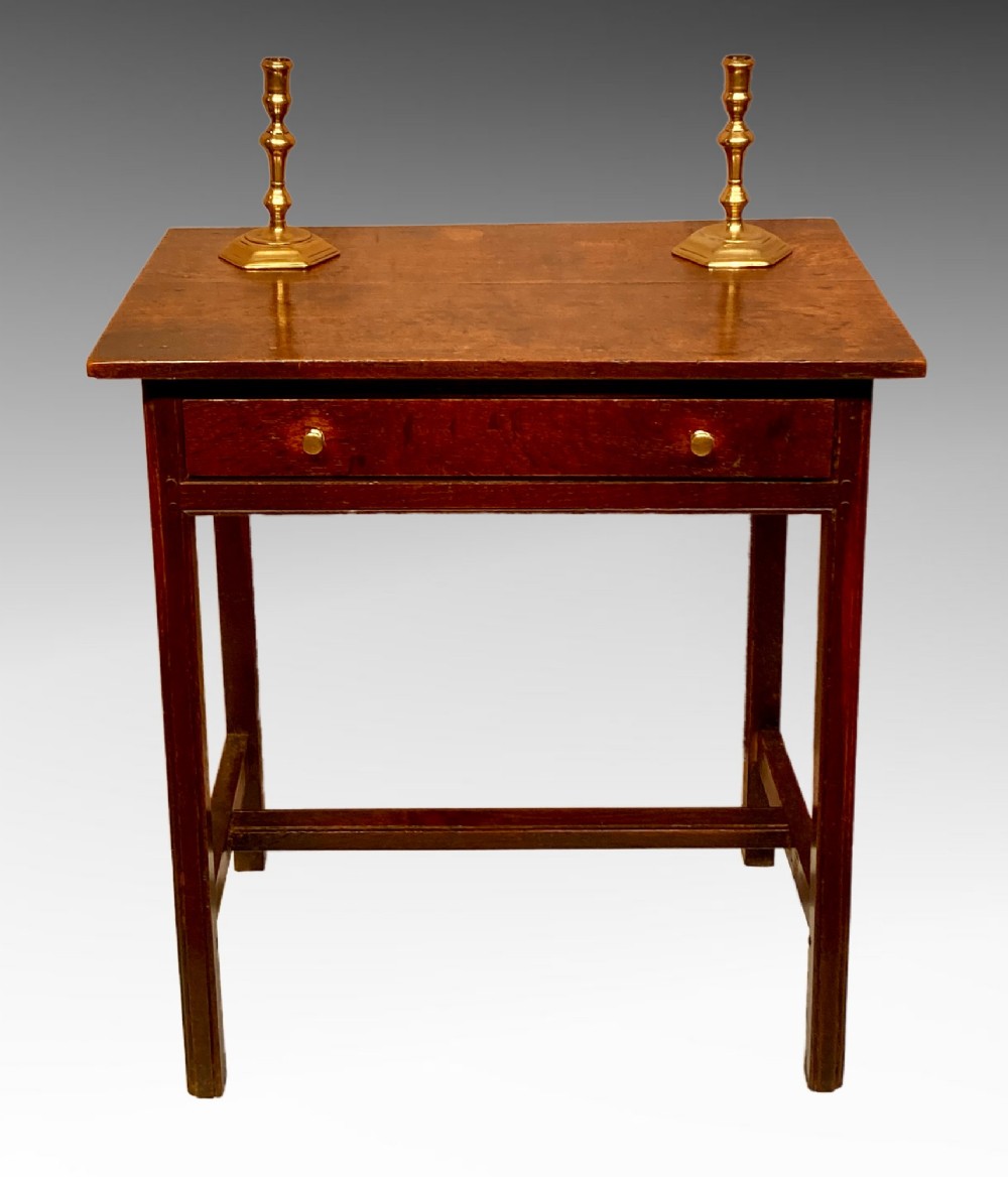 An antique dark oak side table featuring a single drawer with two small brass knobs and square legs connected by stretchers.
