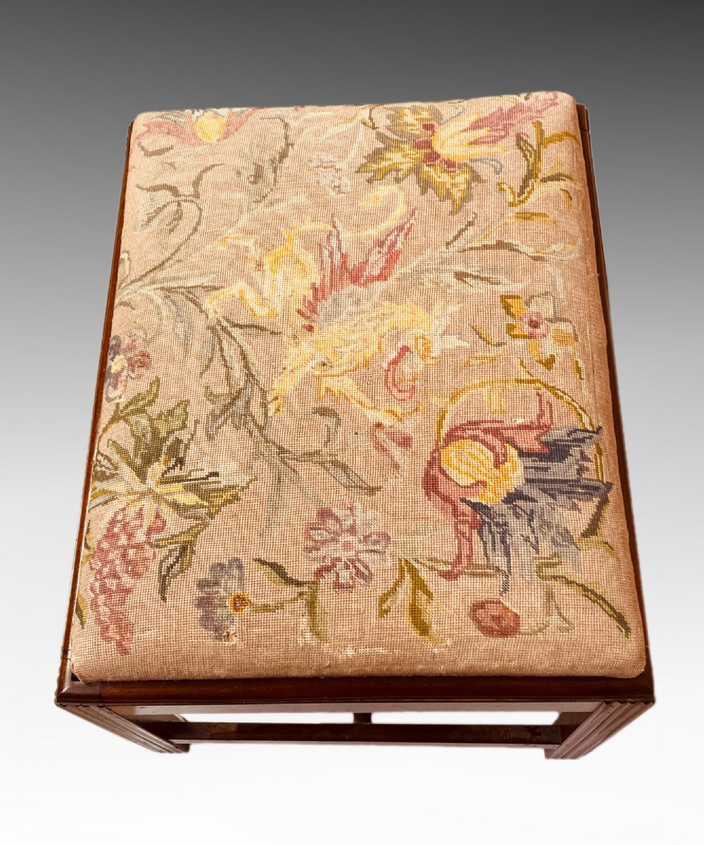 An antique mahogany rectangular dressing stool featuring fluted legs, an H-stretcher base, and a padded floral tapestry seat. View V