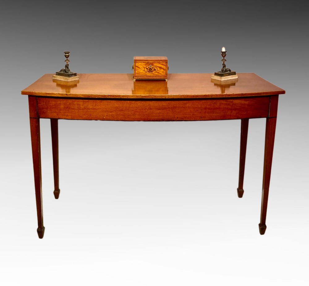 A Georgian mahogany side table featuring a gently curved bow front and four slender square-tapered legs terminating in spade feet.