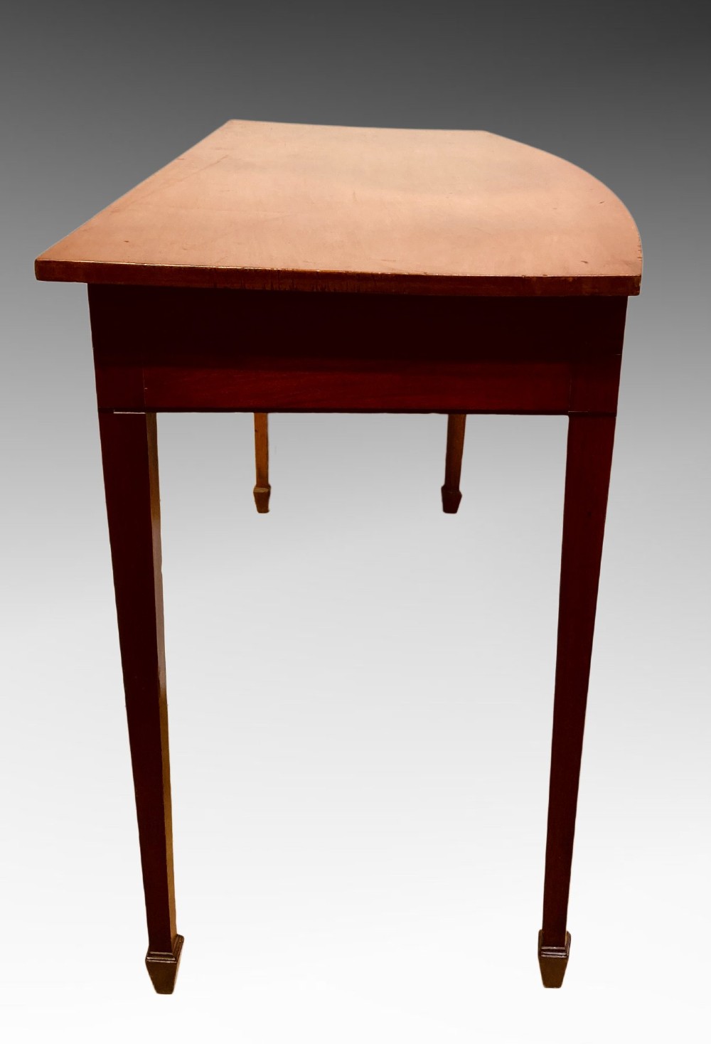 A Georgian mahogany side table featuring a gently curved bow front and four slender square-tapered legs terminating in spade feet. View VI