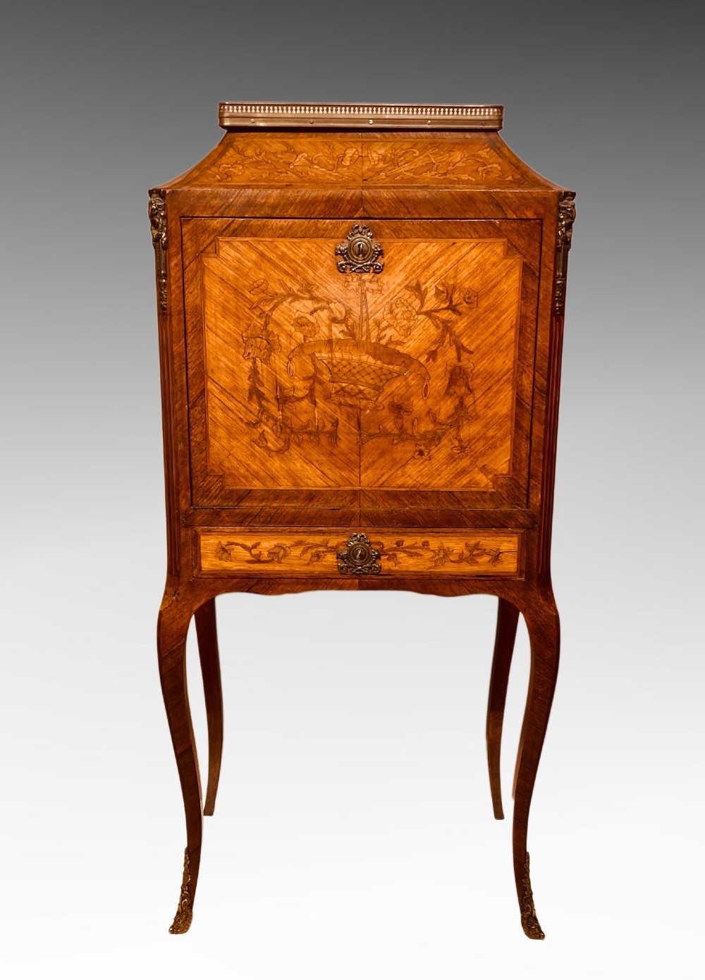 A French Louis XV style kingwood escritoire featuring floral marquetry inlay, slender cabriole legs, a brass top gallery, and gilt-bronze mounts.