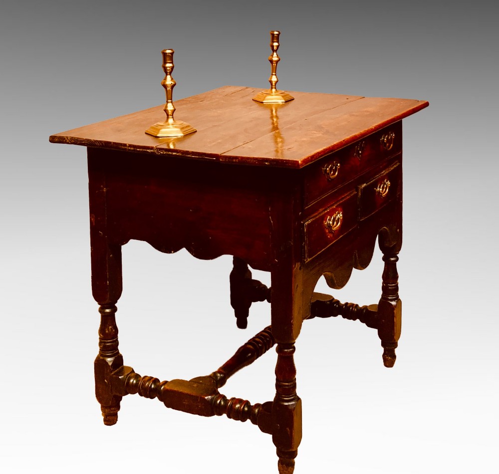 An antique dark elm Queen Anne side table featuring two small drawers with brass handles, a scalloped apron, turned legs, and cross stretchers.