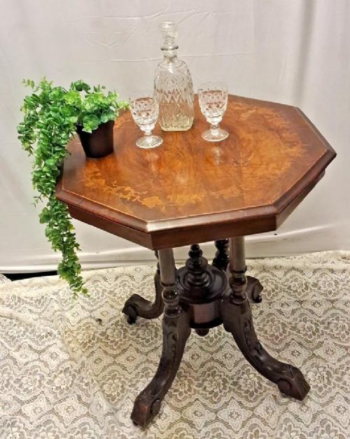 fig 1. An antique octagonal dark wood side table featuring leaf inlay on the top, four turned central columns, a central finial, and four carved splayed legs.