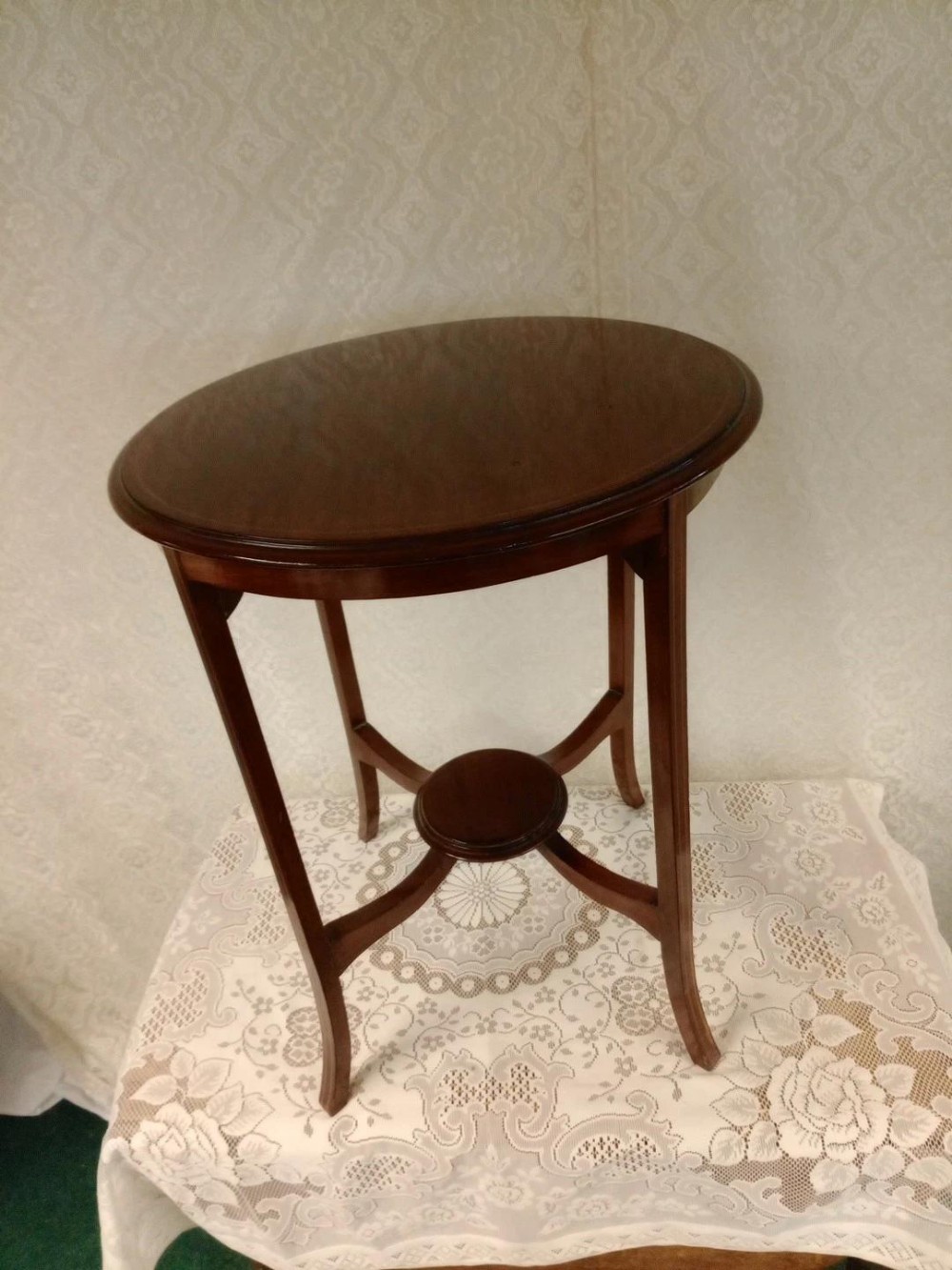 An Edwardian dark mahogany occasional table featuring an oval top surface, four gently curved legs, and a small circular lower tier supported by crossed stretchers.