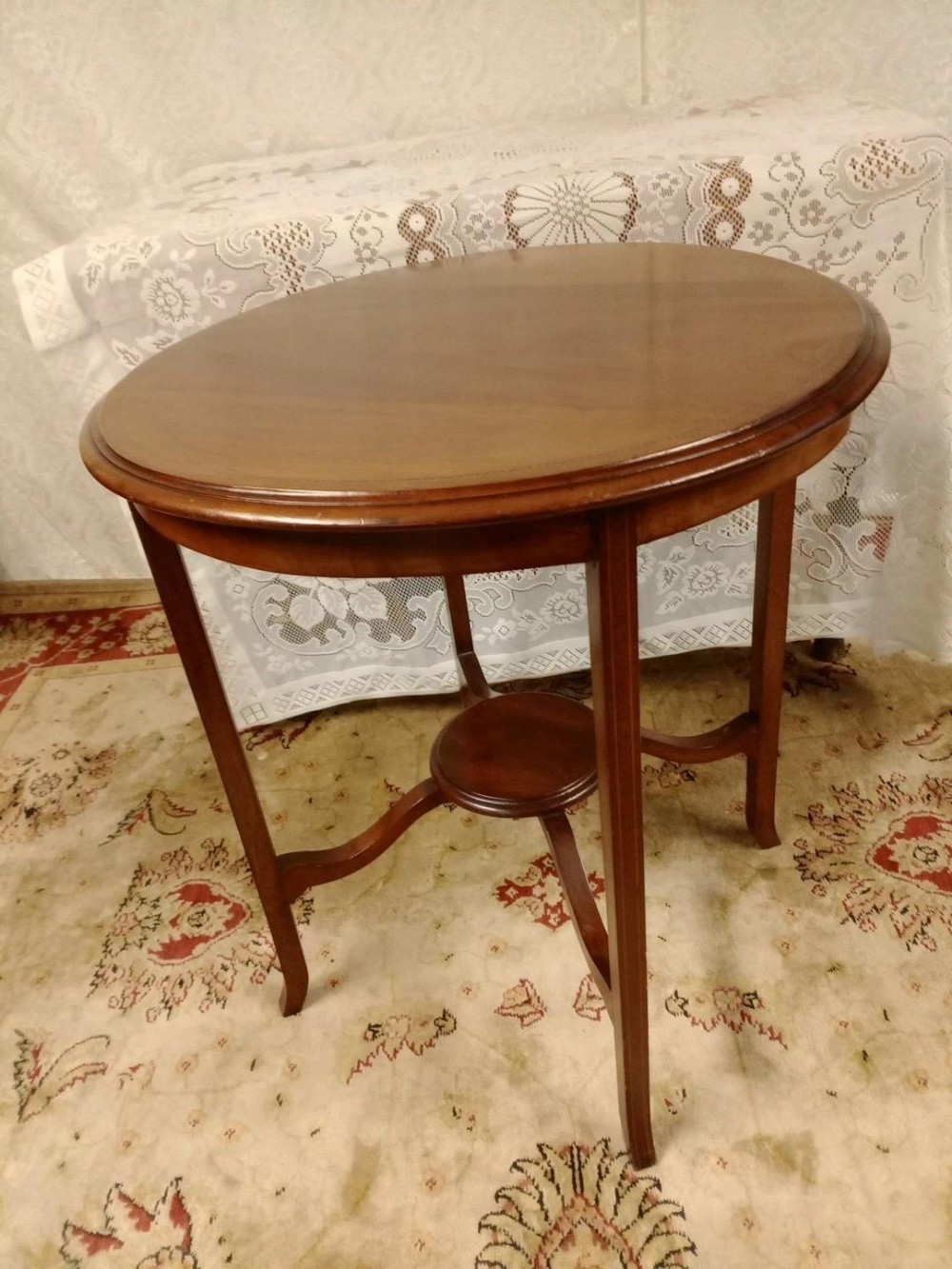 An Edwardian mahogany two-tier occasional table featuring an oval top surface, four slender legs, and a small central circular under-shelf supported by curved stretchers.
