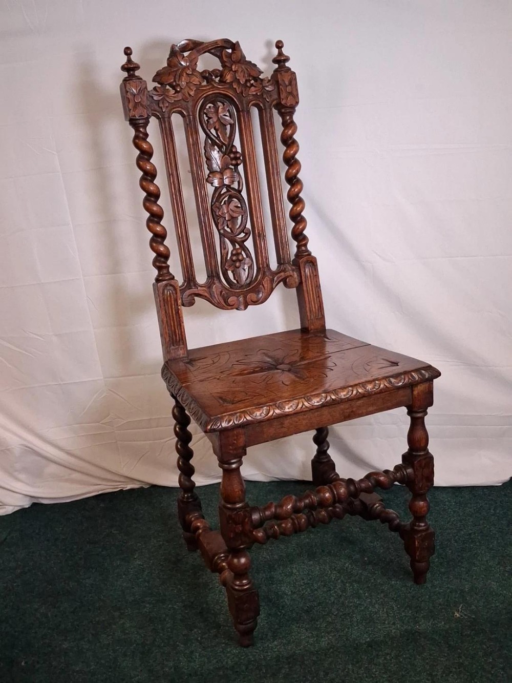 An antique dark oak hall chair with foliate back carvings, barley twist uprights, turned legs, and a carved wooden seat panel.