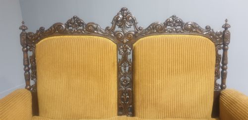 fig 1. An antique double-backed sofa crafted from dark carved walnut wood with mustard yellow striped upholstery and fringe trim.