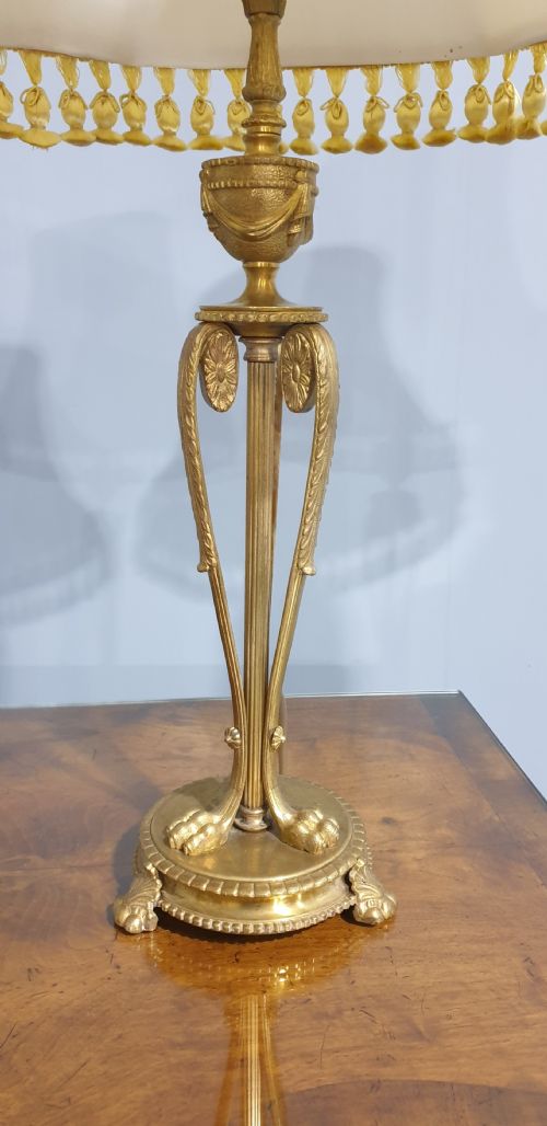 fig 1. A pair of neoclassical gilded ormolu table lamps with slender cast metal bases and cream fabric shades decorated with tassel fringe.