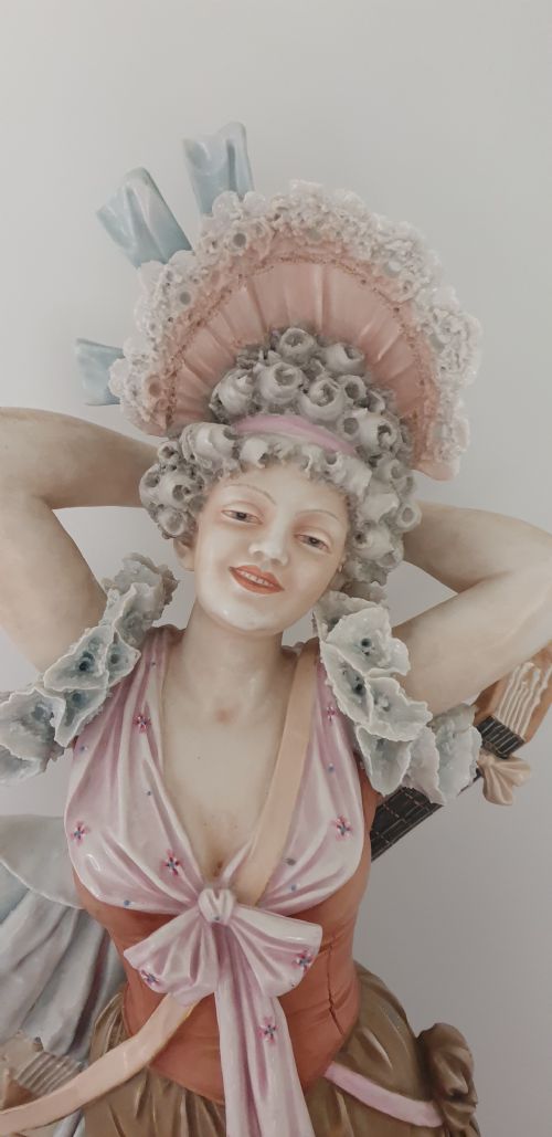 fig 1. A tall Royal Dux porcelain figure of a lady in historical attire holding a musical instrument on an ornate base.