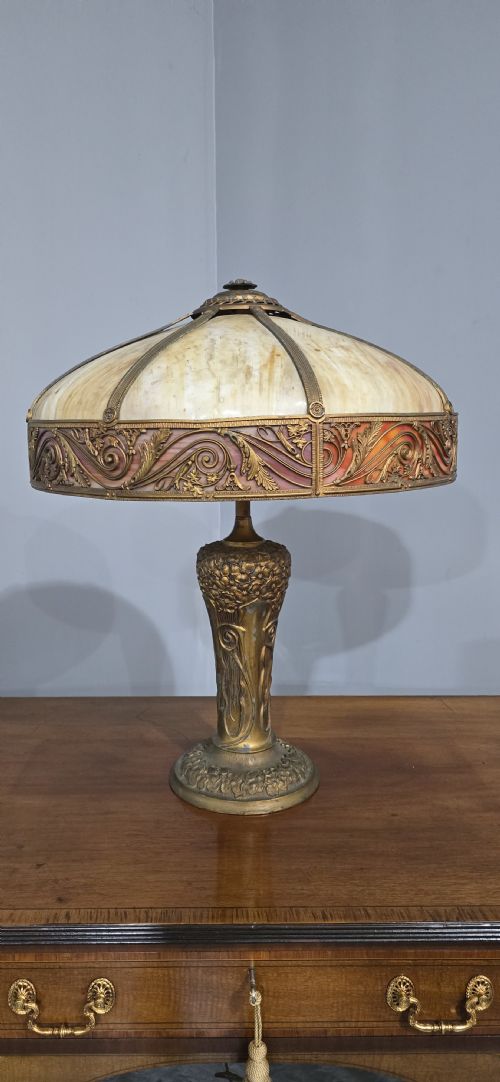 fig 1. An Art Nouveau table lamp featuring a domed amber and red slag glass shade with decorative metal filigree set on a cast bronze floral base.