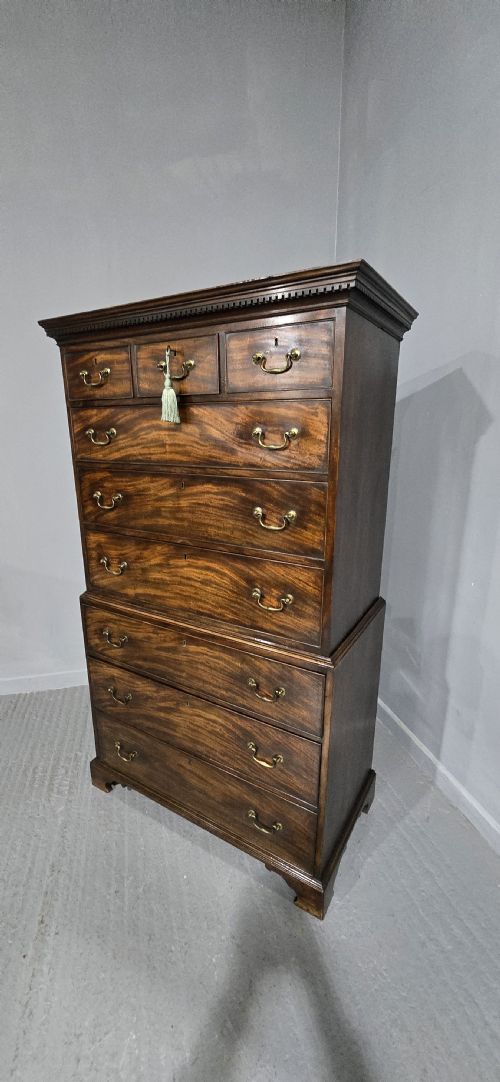 fig 1. A tall Georgian mahogany chest on chest featuring two stacked drawer sections, flame mahogany grain, dentil cornice moulding, brass swan-neck handles, and bracket feet.
