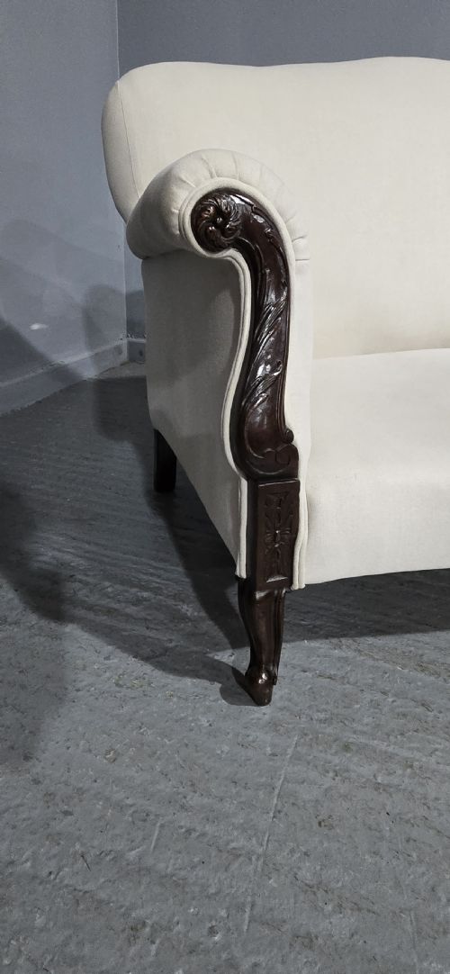fig 1. A Victorian two-seater sofa upholstered in plain cream fabric featuring an arched back, rolled padded arms, and dark carved mahogany front legs.