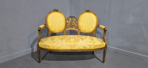 fig 1. An antique French Louis XVI style giltwood two-seat sofa with twin oval medallion backrests, a central carved lyre motif, fluted legs, and yellow silk damask upholstery.