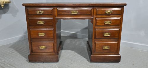 fig 1. A warm brown mahogany pedestal desk featuring a green leather writing top, nine drawers, and brass swan-neck handles set upon twin plinth bases.
