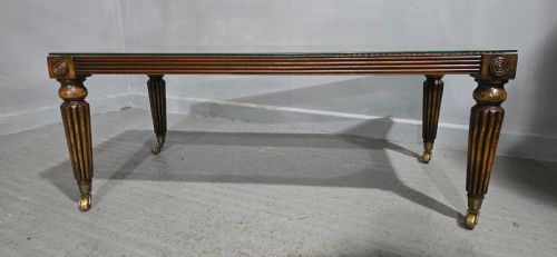 fig 1. A low rectangular mahogany coffee table featuring a glass-covered woven cane top, reeded frieze, carved corner rosettes, and tapered reeded legs terminating in brass castors.