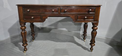 fig 1. A William IV freestanding mahogany desk featuring a leather writing surface, five drawers with wooden knob handles, and turned legs on brass castors.
