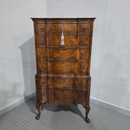 fig 1. A tall Queen Anne burr walnut chest on stand featuring a serpentine contoured front with six drawers, brass drop handles, and carved cabriole legs.