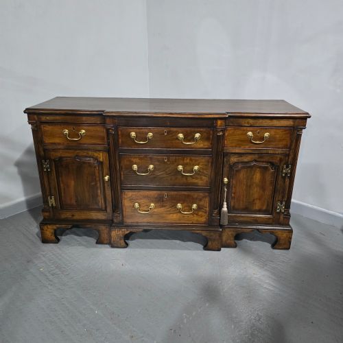 fig 1. A dark oak Georgian breakfront dresser base featuring brass swan-neck handles, three central drawers, and two outer cupboard doors set on bracket feet.