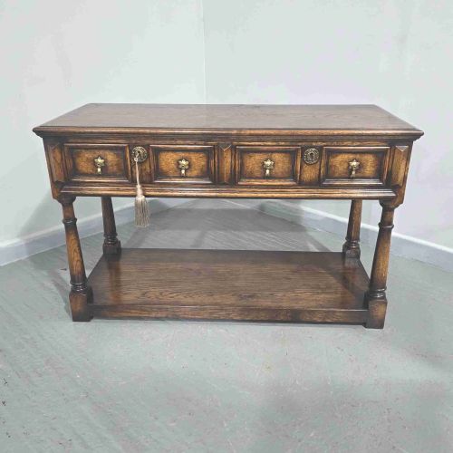 fig 1. An antique dark oak dresser base featuring four panelled drawers with brass drop handles above turned supports and an open lower shelf.