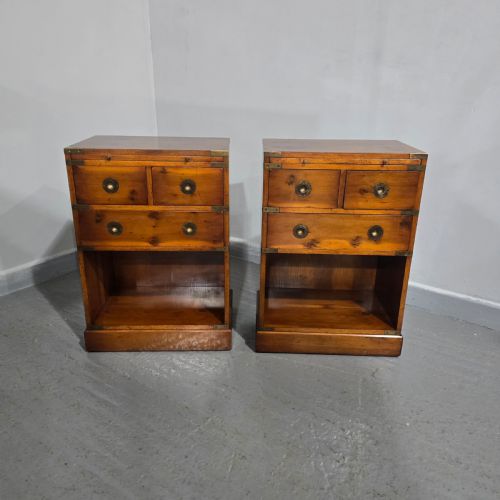 fig 1. A pair of warm brown yew wood campaign style bedside tables featuring brass corner mounts, flush brass pull handles, drawers, and lower open shelves.