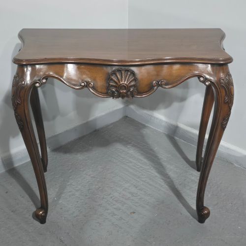 fig 1. A dark mahogany console table featuring a shaped serpentine top, a central shell carving on the apron, and four cabriole legs.
