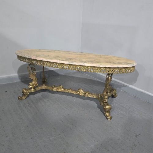 fig 1. An oval gilt brass coffee table with an ornate pierced gallery apron, scrolled mythical legs, a central stretcher, and a polished veined pink marble top.