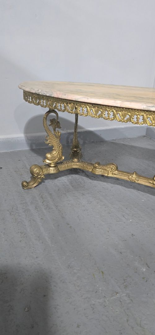 An oval gilt brass coffee table with an ornate pierced gallery apron, scrolled mythical legs, a central stretcher, and a polished veined pink marble top. View VI